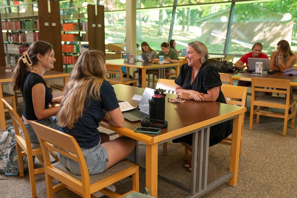 Students and Student Success Director Sara Haviland talk in the library at a table