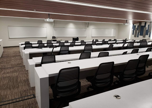 A lecture hall in Albertus Magnus Science Building with long white tables lined with swivel computer chairs, 最高一层在后面, 所有人都面对着房间低前面的白板.