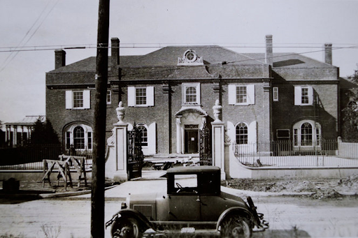 Black and white photo of the Brookby Estate with an early model of car parked out front. 