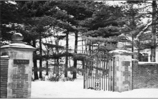 Black and White photo of a wrought iron gate with brick pillars on either side connected to brick walls. 树填满了敞开的大门后面的空间.