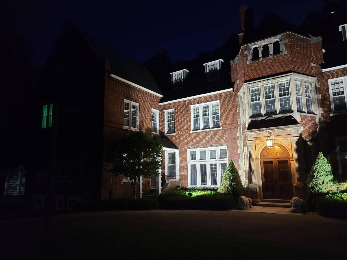 The front of Holmdene Manor at night, with up-lighting and a glowing green light in the window