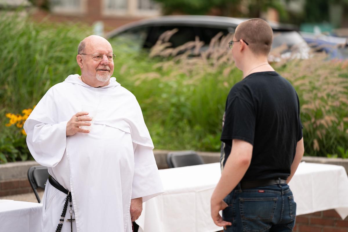 Father Stan in his white robes speaks to a student outside