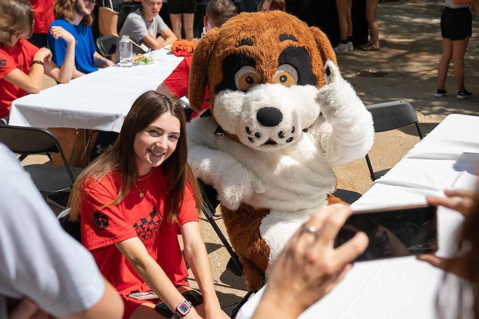 Student posing beside Saint Bernard Mascot Nelson who gives a thumbs up